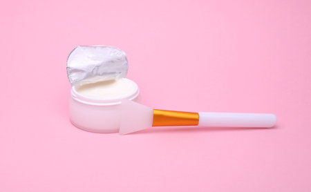 White open cream jar with spatula on pink background.の写真素材