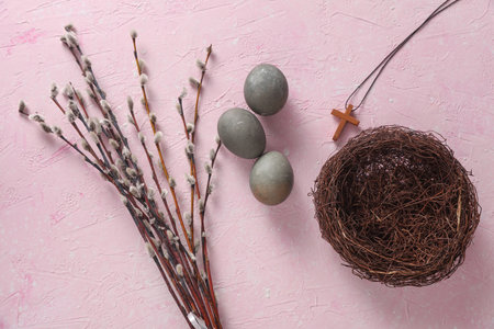 Easter eggs, nest with Christian cross and pussy willow branches on pink concrete background. Top...