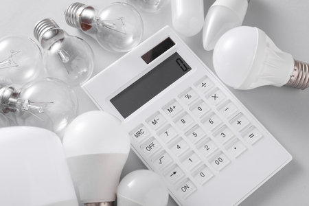 LED and ncandescent light bulbs with calculator on gray background. Saving electricityの写真素材