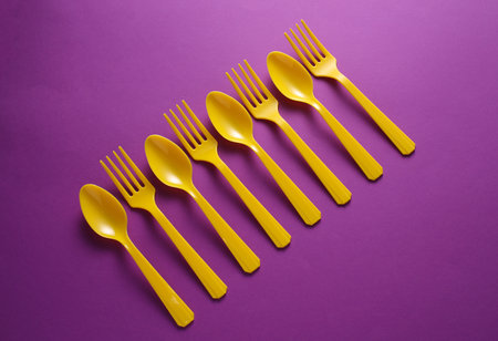Yellow Plastic forks and spoons on purple background