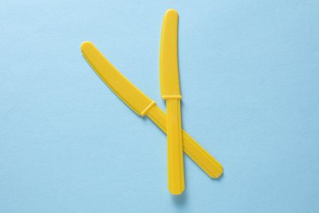 Yellow Plastic knives on blue backgroundの写真素材
