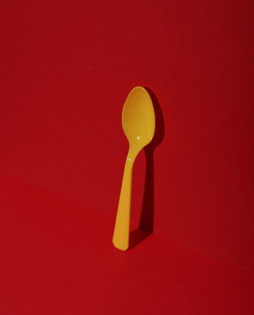 Yellow Plastic spoon on red background with shadow. Minimalism. Creative layout. Food concept