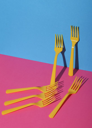 Yellow Plastic forks on pink blue background with shadow. Minimalism. Creative layout. Food concept