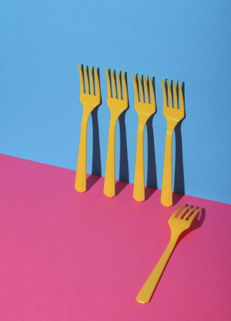 Yellow Plastic forks on pink blue background with shadow. Minimalism. Creative layout. Food conceptの写真素材