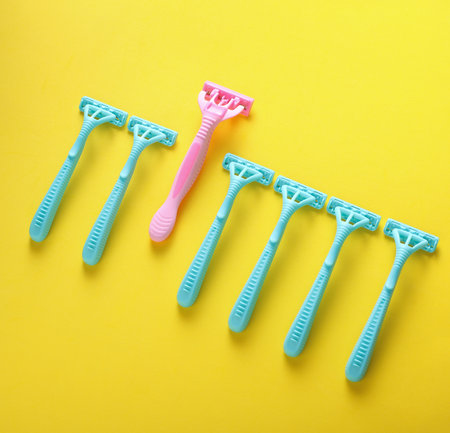 Blue and pink disposable razors on yellow background