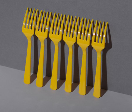 Yellow Plastic forks on gray background with shadow. Minimalism. Creative layout. Food concept