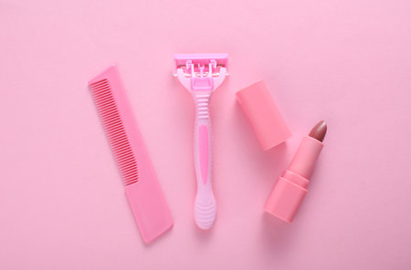 Personal hygiene items. Razor and comb, lipstick on pink background. Top viewの写真素材