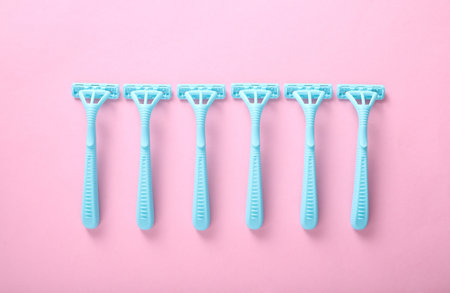 Blue plastic razors on a pink background. Top view