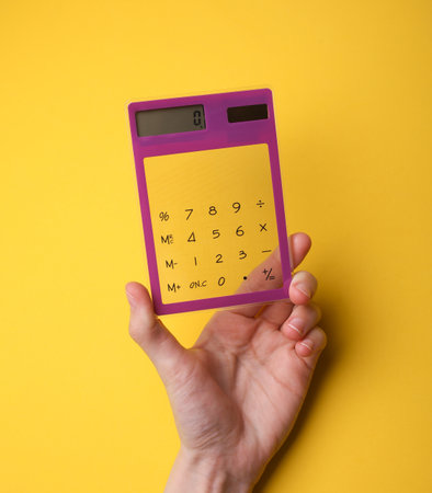 Hand holding calculator on yellow backgroundの写真素材