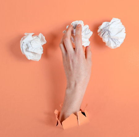 Female hand holds crumpled balls of paper through torn pink paper. Minimalistic idea business conceptの写真素材