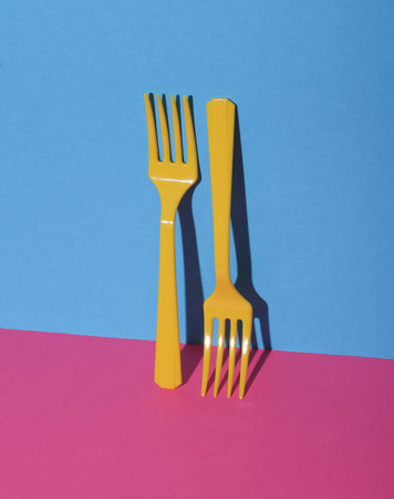 Yellow Plastic forks on pink blue background with shadow. Minimalism. Creative layout. Food concept