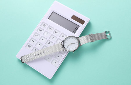 Calculator with wristwatch on mint green background