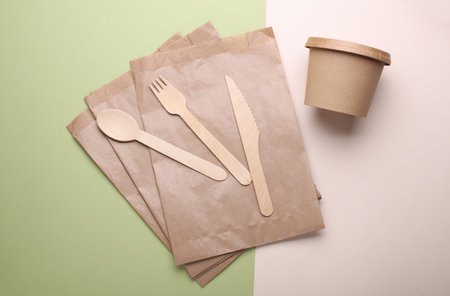 Paper bag with wooden fork, spoon and knife, round box on green beige background. Eco conceptの写真素材