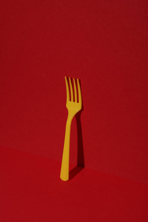 Yellow Plastic fork on red background with shadow. Minimalism. Creative layout. Food conceptの写真素材