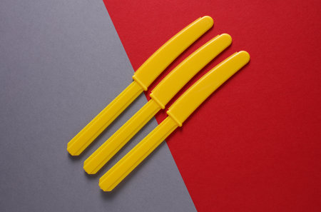 Yellow Plastic knives on gray red background. Minimalism. Creative layoutの写真素材