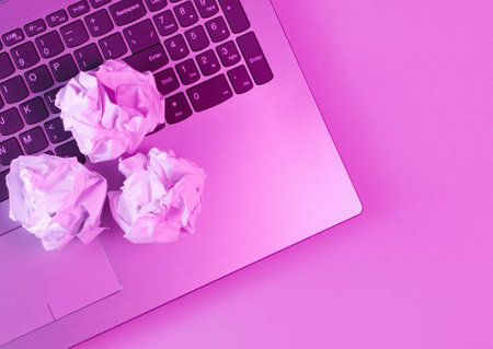 Laptop, crumpled paper balls close up. Holographic pink light. Modern business concept.の写真素材