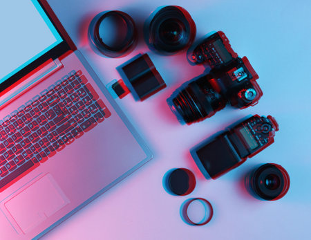 Equipment professional photographer. Laptop, camera, lenses, flashes, light filters. Neon light. Glitch effect. Top viewの写真素材