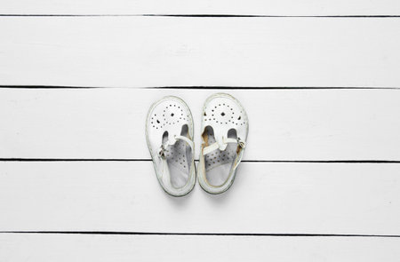 White leather children's sandals on white wooden background. Top view