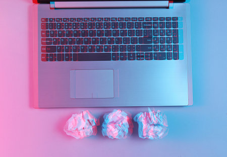Laptop, crumpled paper balls close up. Neon light. Modern business concept. Glitch effect