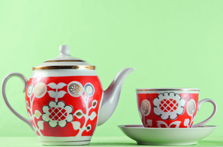 Antique ceramic cup and teapot on wooden table against green wallの写真素材