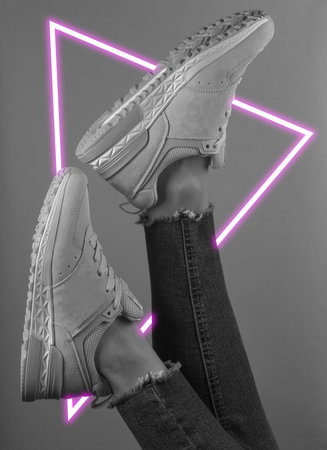 Woman's legs up in jeans and sneakers. 80's synth wave and retrowave glowing triangle futuristic...