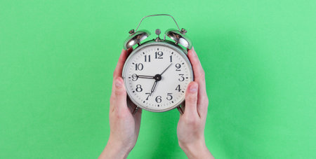 Female hands hold retro alarm clock on green background