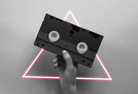Hand holding video cassette. 80's synth wave and retrowave glowing triangle futuristic aesthetics. Old fashioned abstraction conceptの写真素材