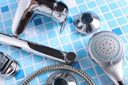Parts of disassembled bathtub faucet with shower on tile background