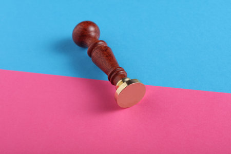 Vintage personal stamp with wooden handle and bronze head on blue pink background. Top view