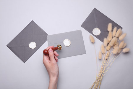 Girl sealing envelope with wax sealing stamp on gray background