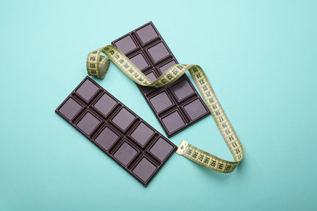 Dark chocolate bars with measure tape on blue background. Calorie counting, diet, weight lossの写真素材