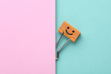 Binder clip with a smiling face on a pink blue backgroundの写真素材