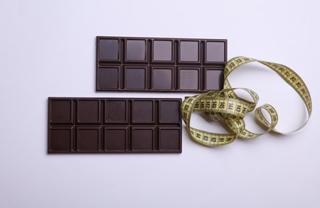 Dark chocolate bars with measure tape on white background. Calorie counting, diet, weight lossの写真素材
