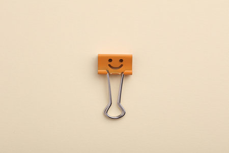 Binder clip with a smiling face on a beige background