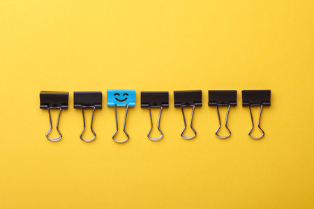 Binder clip with smiling face and faceless binders on yellow background.の写真素材