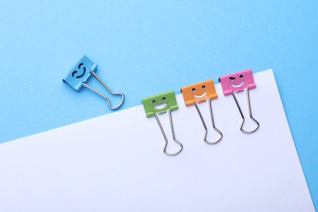 Binder clips with a smiling faces and paper sheet on blue background. Business conceptの写真素材