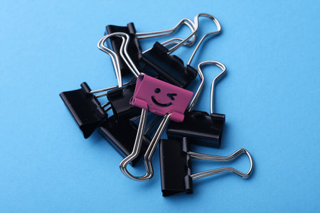 Binder clip with smiling face and and faceless binders on blue background. Leadership, uniqueness, career growth. Business concept.の写真素材