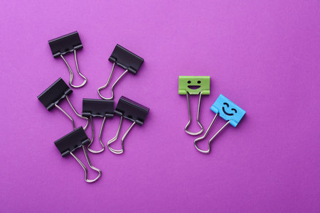 Binder clip with smiling face and faceless binders on purple background. Leadership, uniqueness, career growth. Business concept.の写真素材
