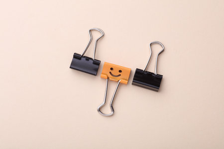 Binder clip with smiling face and faceless binders on beige background.