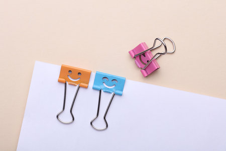Binder clips with a smiling faces and paper sheet on beige background. Business conceptの写真素材