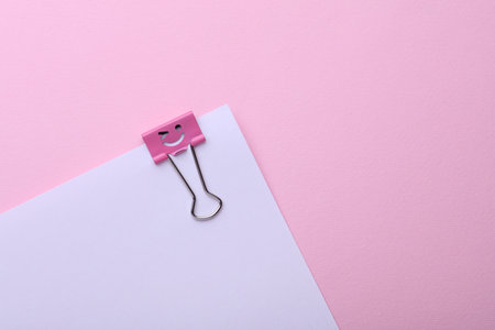 Binder clip with a smiling face and paper sheet on pink backgroundの写真素材