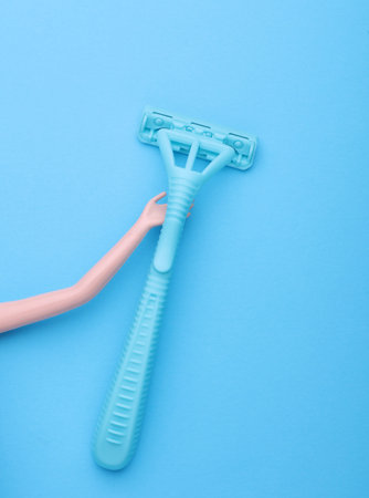 Dolls hand holding plastic razor on blue backgroundの写真素材