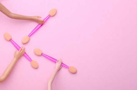 Doll's hands holding makeup sticks on pink backgroundの写真素材