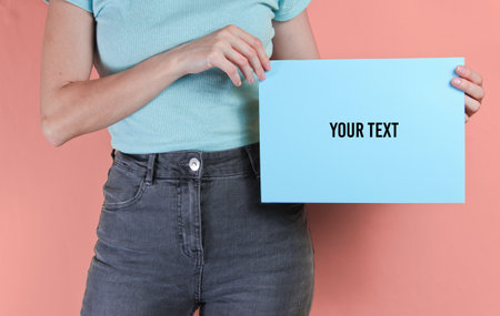 Woman holding blue empty sheet of paper for copy space on pink background. Crop photo, studio shot