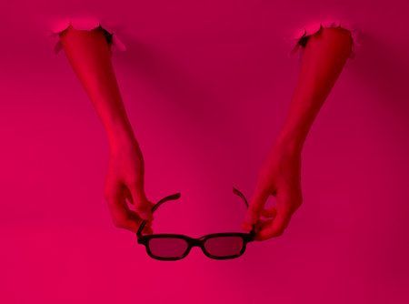 Women's hands hold 3D glasses through the torn holes with pink neon light. Creative artの写真素材