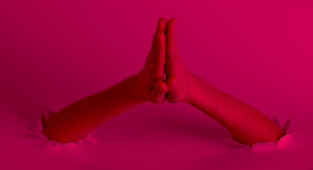 Women's hands pray through the torn holes with pink neon light. Creative artの写真素材