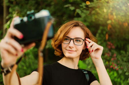 Young attractive female tourist takes selfie portrait on retro camera outdoors
