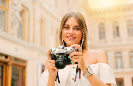 Young attractive tourist woman with a retro camera in her hands while posing at urban old architecture. Discover new placesの写真素材
