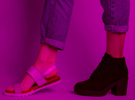 Female legs in jeans shod in boot and sandal. Pink neon light. Seasonal shoes. creative fashion shot