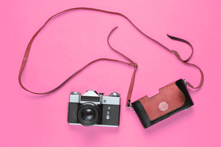 Tourist minimalism concept. Vintage retro film camera and leather cover with strap on pink background. Top viewの写真素材